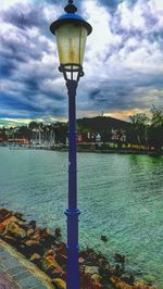 Street light by river against buildings in city against sky