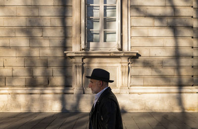 Side view of adult man in hat and leather jacket walking against wall on street. madrid, spain