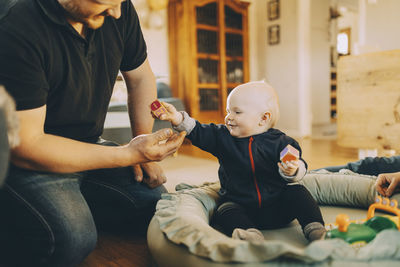 Smiling male toddler giving toy block to father sitting in living room at home