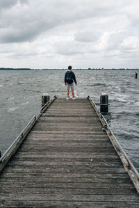 Man standing on jetty leading towards sea against sky