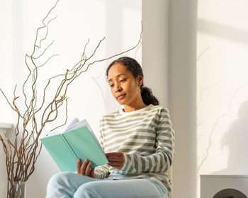 African-american female peacefully reading book in lounge. enjoying moment. slow living lifestyle