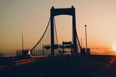 Cars moving on bridge against sky during sunset