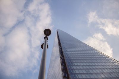 Low angle view of street light by modern building against sky