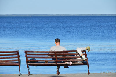 Rear view of man sitting on shore against sea