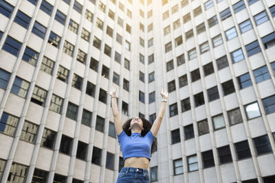 Carefree woman with arms raised in front of building