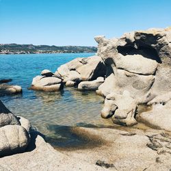 Statue on rock by sea against clear blue sky