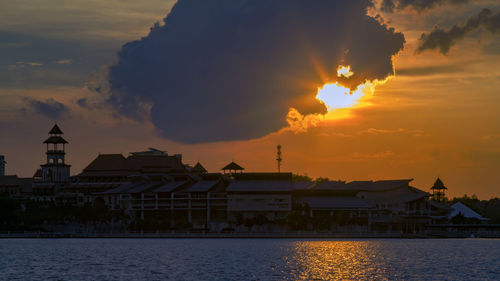 Silhouette buildings by sea against sky during sunset