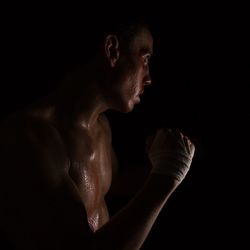 Side view of shirtless athlete against black background