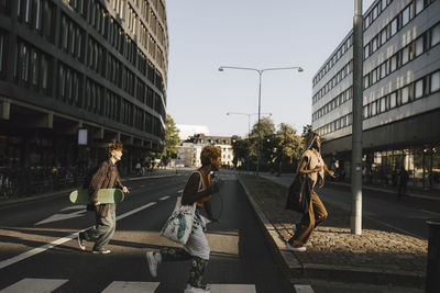 Happy multiracial friends running while crossing street in city