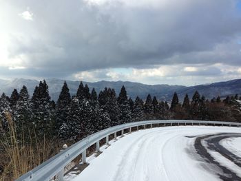 Snow covered road by trees against sky