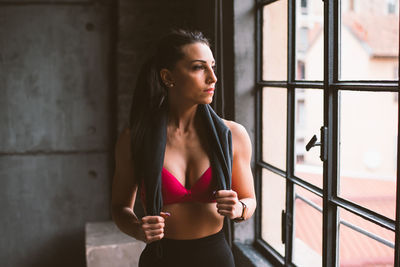 Woman looking away while standing against window