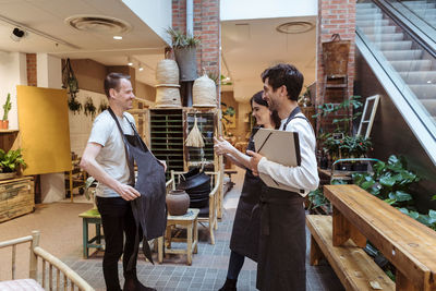 Man and woman smiling while looking at male colleague wearing apron in boutique