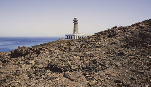 Lighthouse on beach by sea against sky