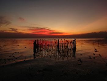 Wooden posts on beach against sky during sunset