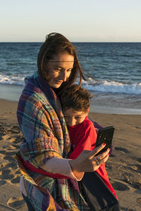 Mother and son doing selfie while standing at beach