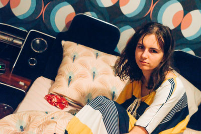 Portrait of teenage girl sitting on bed at home