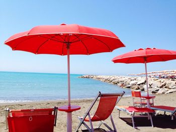 Empty deck chairs and parasols at beach against clear sky