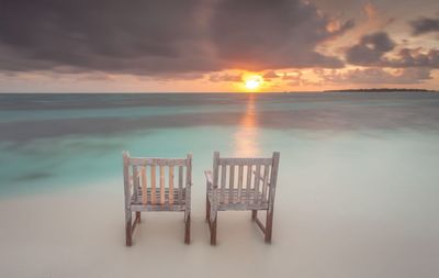 Chairs on beach against cloudy sky during sunset