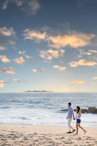 Couple standing on beach against sky