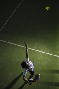 Male athlete servicing ball while playing padel tennis in sports court at night