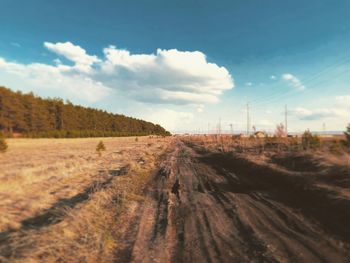 Dirt road amidst field against sky