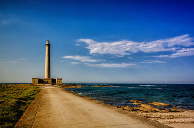 Lighthouse by sea against blue sky