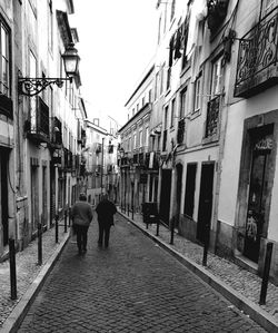 Rear view of people walking on road along buildings