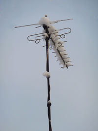 Low angle view of antenna on pole covered with snow against sky