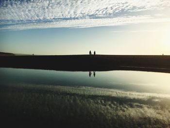 Silhouette man by lake against sky during sunset