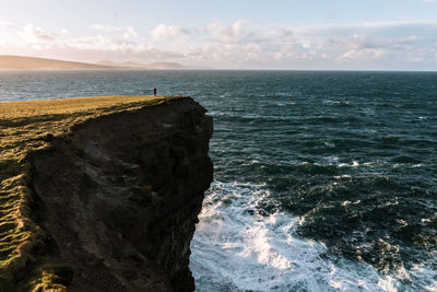 Distant view of person standing on cliff by sea