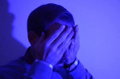 Close-up of man covering eyes in illuminated room