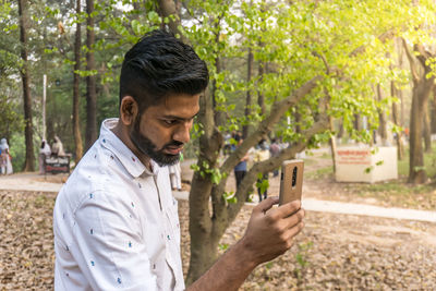 Young man using mobile phone while standing on tree