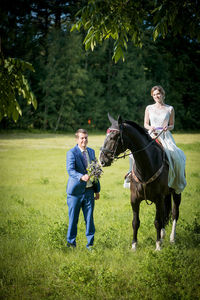 Bridegroom walking by bride riding horse on grass