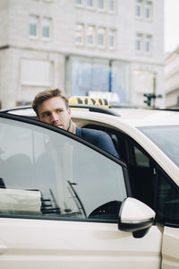 Businessman looking away while coming out of taxi during business trip in city
