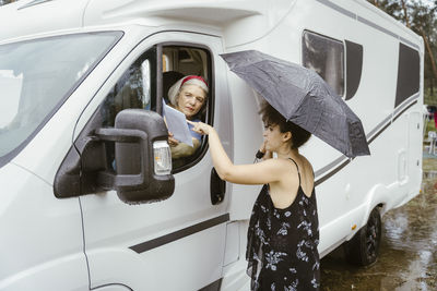 Young woman with umbrella helping senior woman for direction