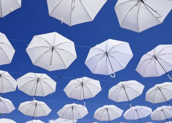 White umbrellas hanging against a blue sky over a fountain square with fountains 