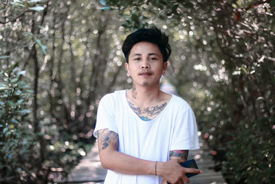 Portrait of young man standing against trees