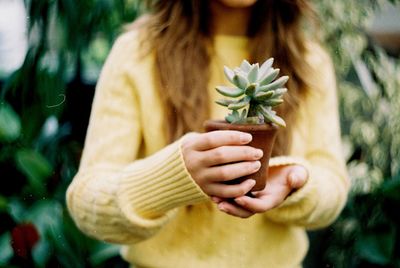 Midsection of woman holding potted plant at yard