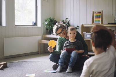 Smiling senior female teacher showing circle shape boy in classroom at kindergarten