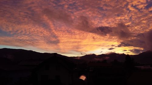 Silhouette houses against dramatic sky during sunset