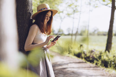 Young woman leaning against tree trunk using smartphone