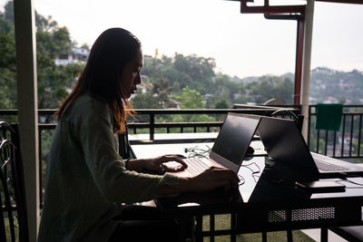 Side view of young female freelancer on vacation in casual clothing working with laptop at outdoors terrace of restaurant at sri lanka