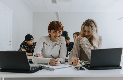 Cheerful female students studying together at desk in classroom