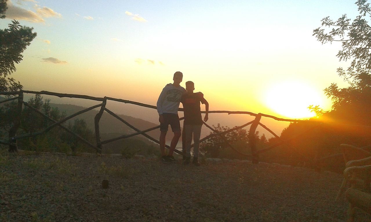 sunset, lifestyles, sun, leisure activity, orange color, silhouette, full length, men, sky, standing, tranquility, beauty in nature, rear view, scenics, nature, tranquil scene, sunlight, person