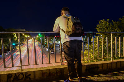 Rear view of man standing on illuminated street against sky at night