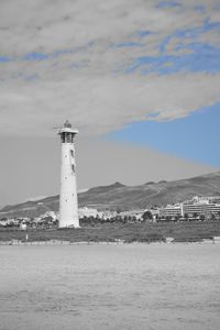 Lighthouse by sea and buildings against sky