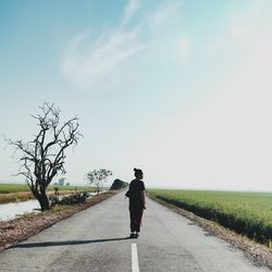 Rear view of woman standing on road against sky