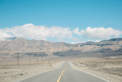 Empty road by mountains against sky