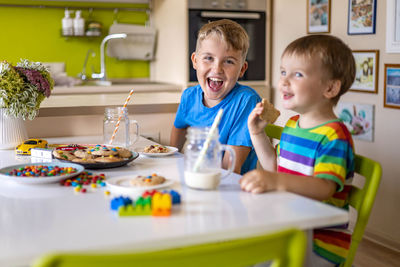 Cheerful boy with brother eating breakfast at home