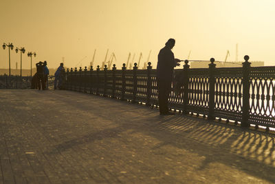 Rear view of people walking on footbridge against sky during sunset